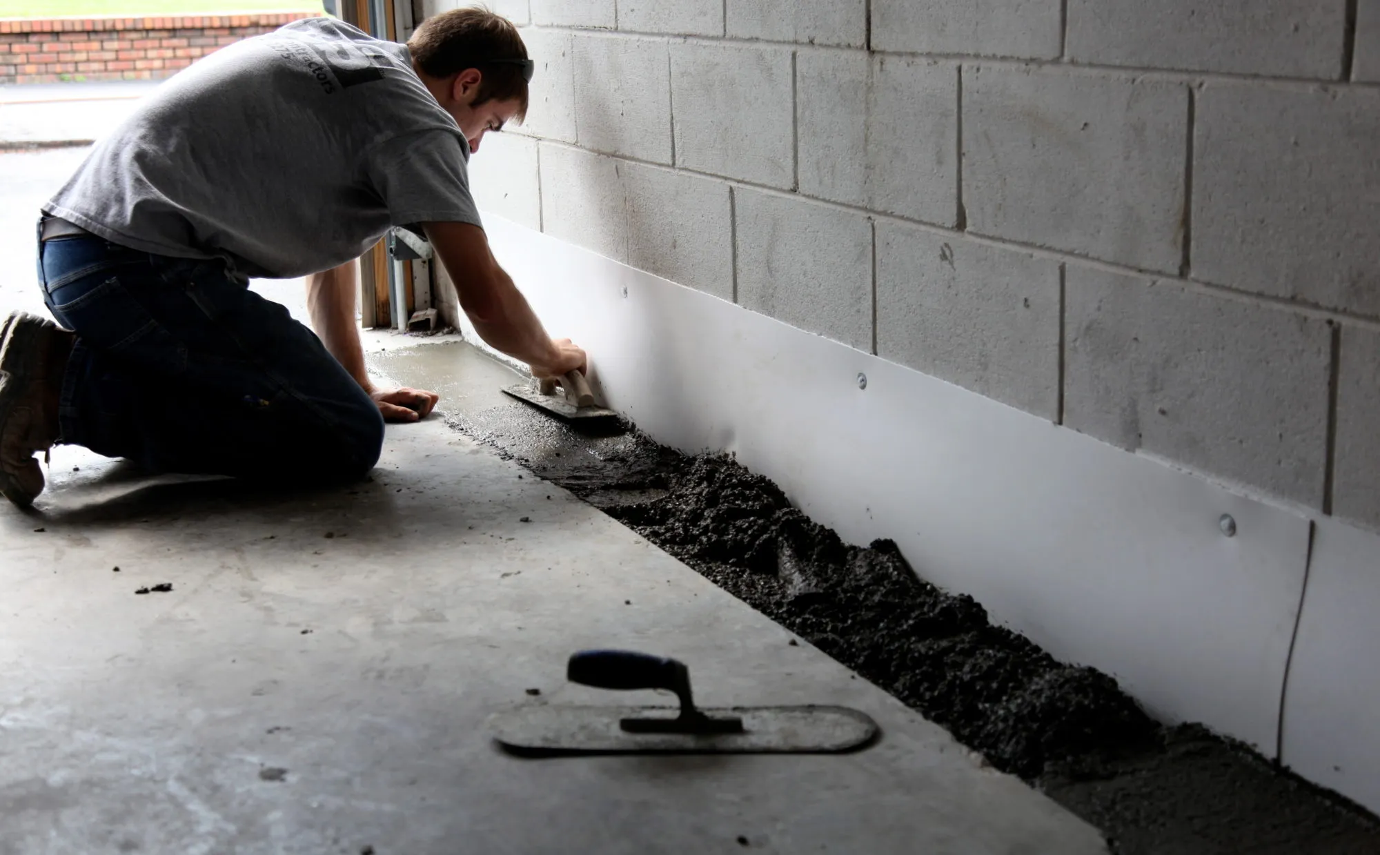 Contractor applying interior waterproof coating along a basement wall and floor joint